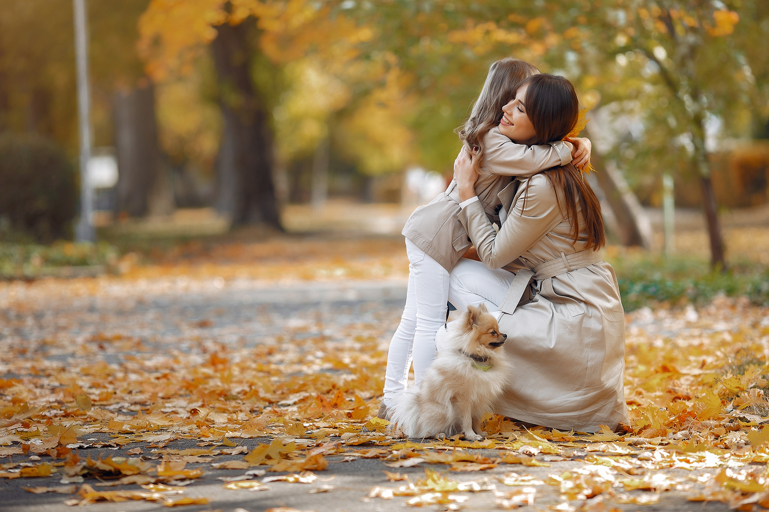 Happy woman hugging little girl in park in autumn day